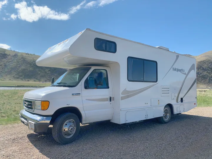 White Ford E350 Majestic RV rental parked on a gravel lot beside a river with green hills under a blue sky.. Majestic Leisure Craft Tourer Ii 2007