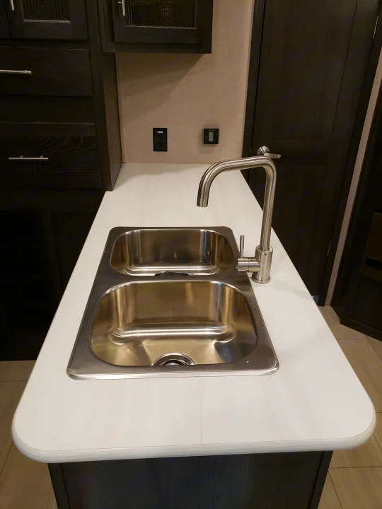RV rental kitchen: modern stainless steel double sink, high-arc faucet, white countertop, and dark wood cabinets. Includes climate control.. Forest River XLR hyperlite 2019
