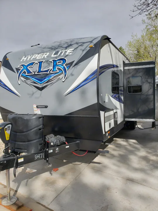 A grey and blue Hyper Lite XLR travel trailer/toy hauler RV, perfect for your next rv rental getaway. Door open, ready to explore.. Forest River XLR hyperlite 2019