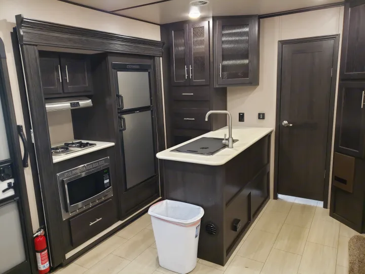 Clean, modern RV rental kitchen. Features dark cabinets, fridge, microwave, stovetop, and island with sink.. Forest River XLR hyperlite 2019