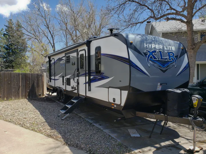This Hyper Lite XLR travel trailer, perfect for an RV rental, is parked on a gravel and concrete driveway on a sunny day.. Forest River XLR hyperlite 2019