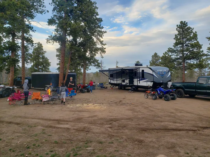 Family camping trip with an RV rental, campfire, and ATVs amidst pine trees under a cloudy sky.. Forest River XLR hyperlite 2019