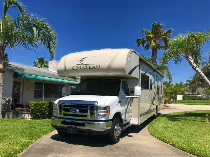 Chateau RV rental parked on a sunny residential driveway amidst vibrant palm trees and green grass, ready for your next adventure.. Thor Chateau 2020