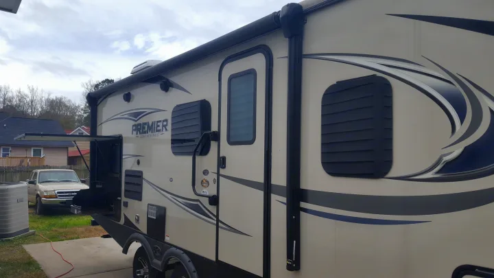 An RV rental: a modern Premier travel trailer with a side grill and awning extended, parked on a driveway.. Keystone RV Bullet Premier 2019