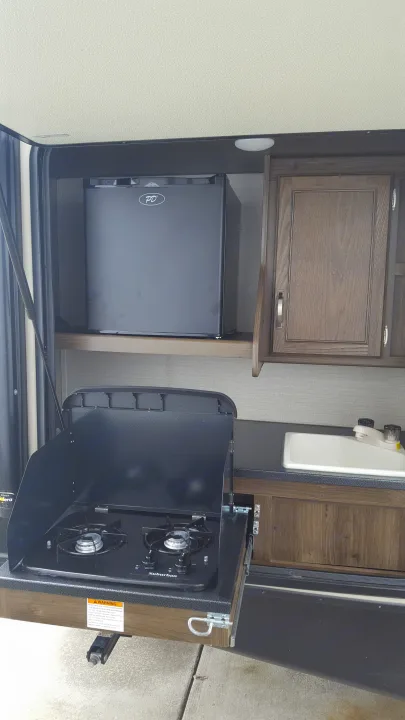 Convenient outdoor kitchen in an RV rental, complete with a mini-fridge, stove, and sink for camping.. Keystone RV Bullet Premier 2019
