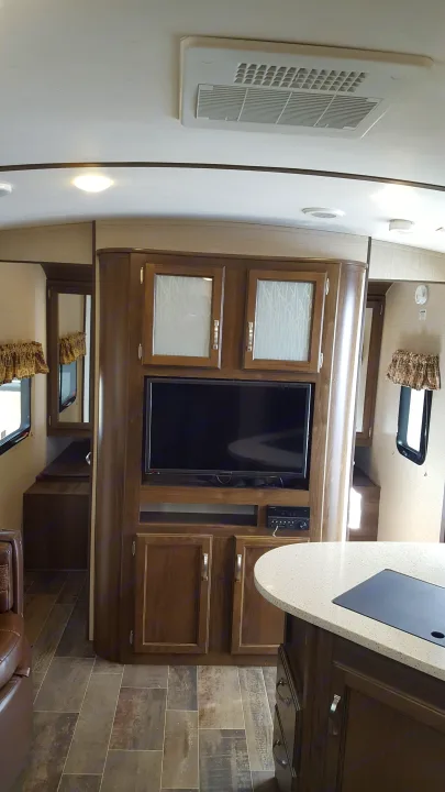 RV rental interior with a cozy living area featuring a TV, wood cabinets, a modern kitchen island, and AC unit.. Keystone RV Bullet Premier 2019