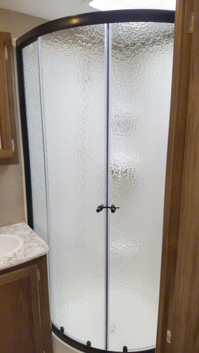 RV rental: Inside a compact bathroom, a curved shower with textured glass doors and black handles stands next to a sink vanity.. Keystone RV Bullet Premier 2019