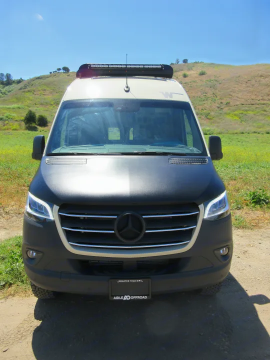 Off-road ready Mercedes-Benz Sprinter RV rental with roof light bar, parked on a sunny dirt path. Ideal adventure van.. Winnebago Revel 2020