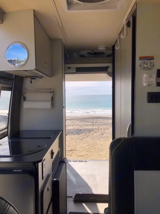 RV rental interior looking out to a sandy beach and ocean, showcasing a modern mobile living space with controls.. Winnebago Revel 2020