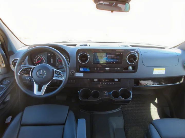 Modern RV rental cockpit: Mercedes-Benz dashboard, steering wheel, infotainment playing radio, and climate controls.. Winnebago Revel 2020