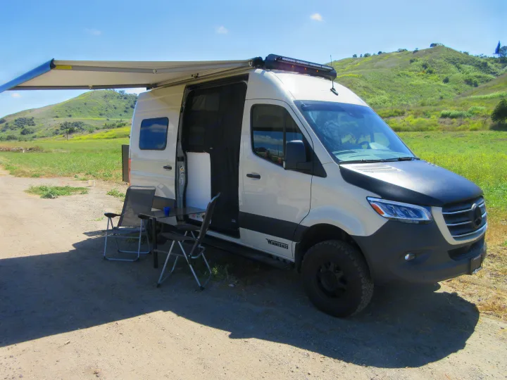 Enjoy nature with this RV rental camper van, featuring an outdoor setup with awning, chairs, and table.. Winnebago Revel 2020