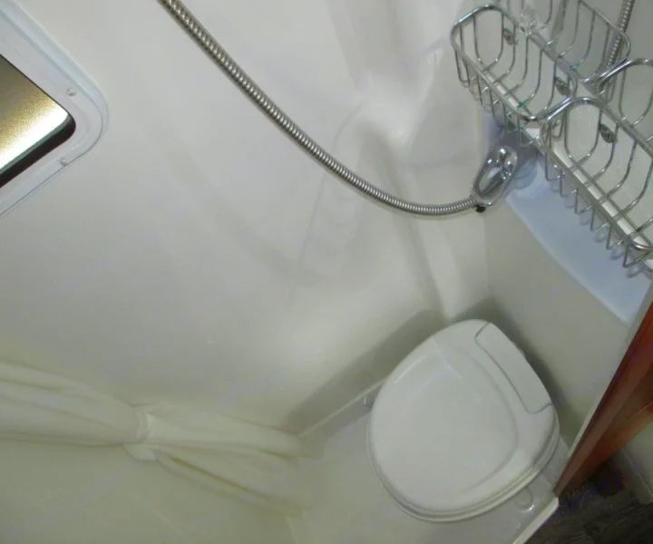 Inside an RV rental: a compact bathroom with a white toilet, shower hose, and metal storage. Roadtrek Ssagile 2014