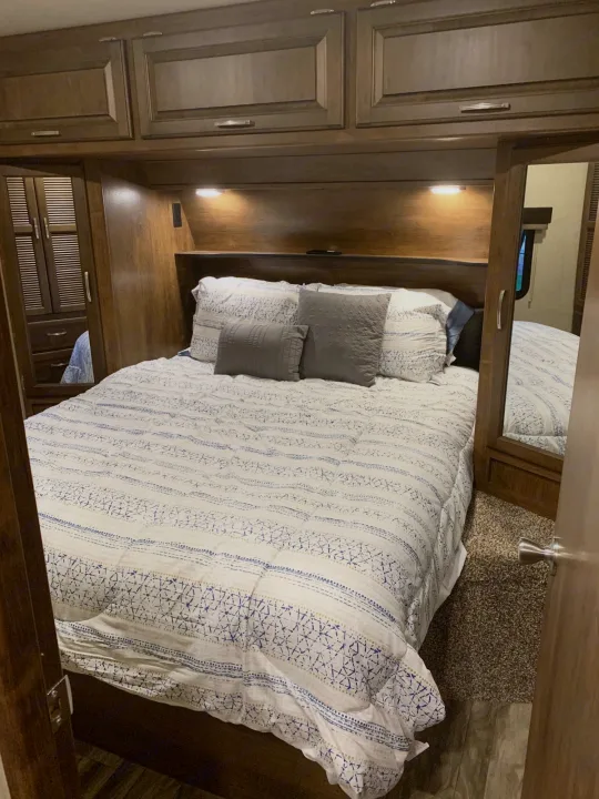 Cozy RV rental bedroom with built-in storage, soft lighting, and a comfy bed. Experience comfortable travel.. Grand Design Reflection 2019
