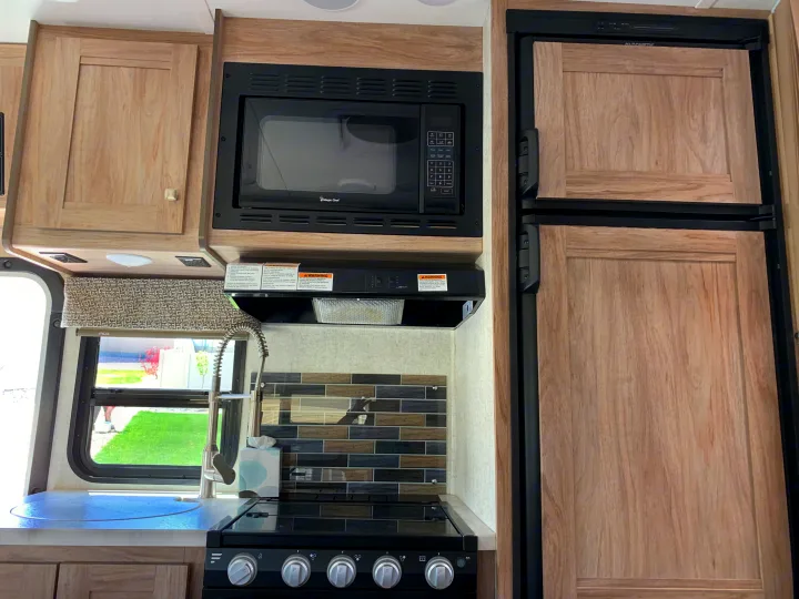 This RV rental kitchen features a microwave, fridge, stove, sink, light wood cabinets, and a tiled backsplash, offering comfort on the go.. Forest River Sunseeker 2019