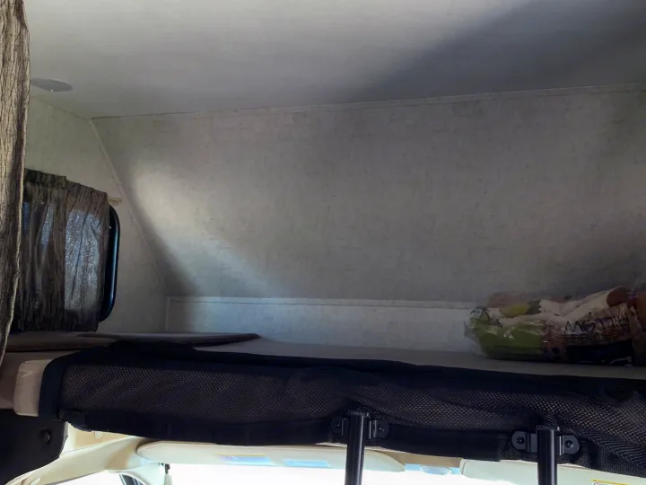 Overhead sleeping area in an RV rental, featuring a safety net and window curtain.. Forest River Sunseeker 2019