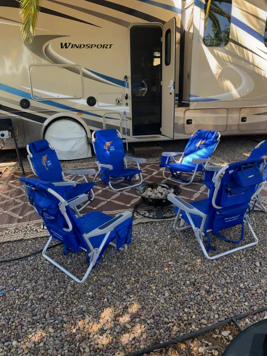 Enjoying an **rv rental** getaway: a cozy campsite with blue Tommy Bahama chairs and a fire pit by a Windsport RV.. Thor Windsport 2018
