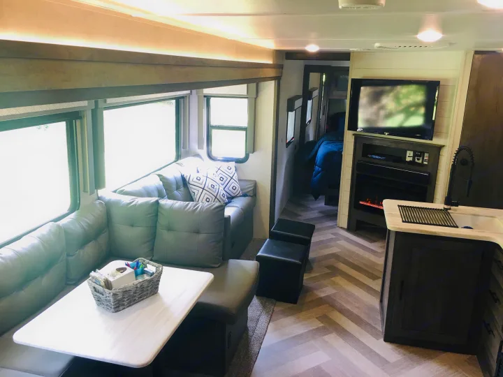 Inside a modern RV rental: a bright living area with dinette seating, large windows, an entertainment center, and a compact kitchen.. Forest River Salem 2021