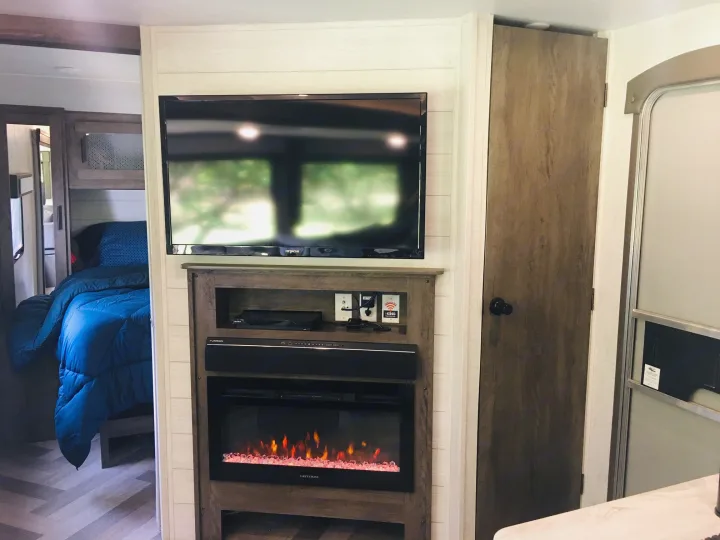 Cozy RV rental living area featuring a TV, electric fireplace, and a glimpse into the bedroom with a blue comforter.. Forest River Salem 2021