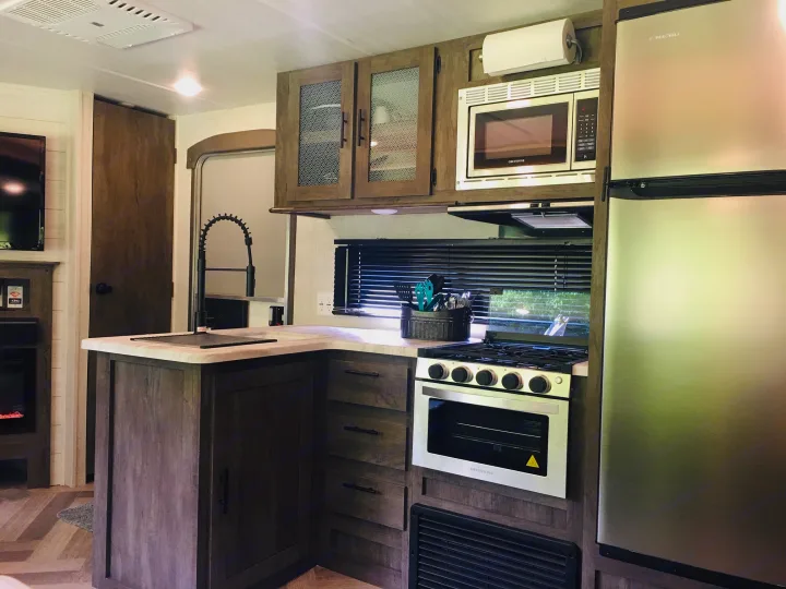 Modern RV rental kitchen with stainless steel appliances, dark wood cabinets & ample counter space.. Forest River Salem 2021