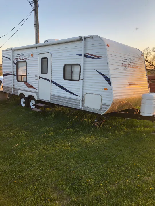 White Jay Flight travel trailer, perfect for an RV rental, is parked on a vibrant green lawn under a sunny sky.. Jayco Jay Flight 2011
