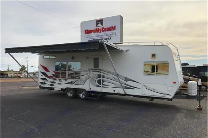 White travel trailer RV with bold graphics and a deployed awning, parked near a 'ShareMyCoach!' rv rental sign.. Weekend Warrior Billet Edition 2006