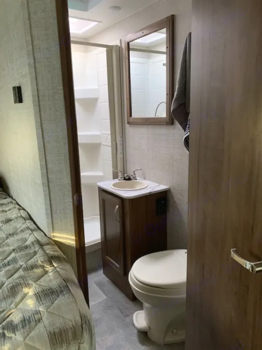 Clean RV rental interior featuring a compact bathroom with a toilet, sink, and shower. Bedroom area visible.. Gulf Stream Conquest 2020