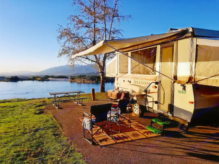 Rockwood pop-up rv rental at a scenic lakefront campsite with outdoor furniture, offering mountain views under a clear sky.. Forest River Rockwood Premier 2013