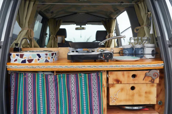 Cozy RV rental kitchen featuring a mosaic sink, stove with pan, and custom wooden drawers for mobile cooking adventures.. Toyota Voxy 2007