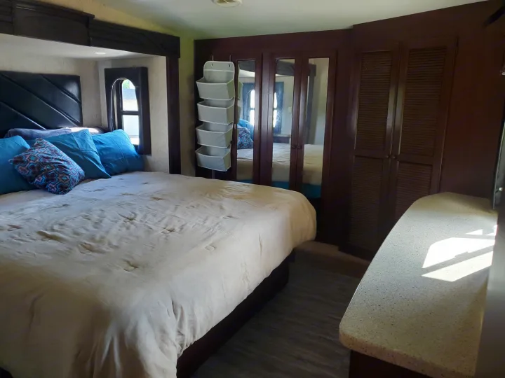 Cozy RV rental bedroom with a comfortable bed, mirrored wardrobe, and practical hanging storage.. Heartland Cyclone 2014
