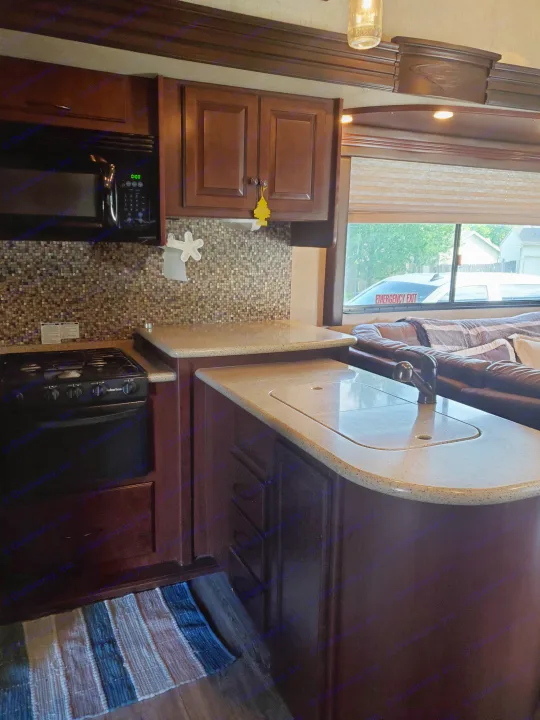 RV rental kitchen and living area, showcasing a compact stove, microwave, sink, and comfy brown leather sofa.. Heartland Cyclone 2014