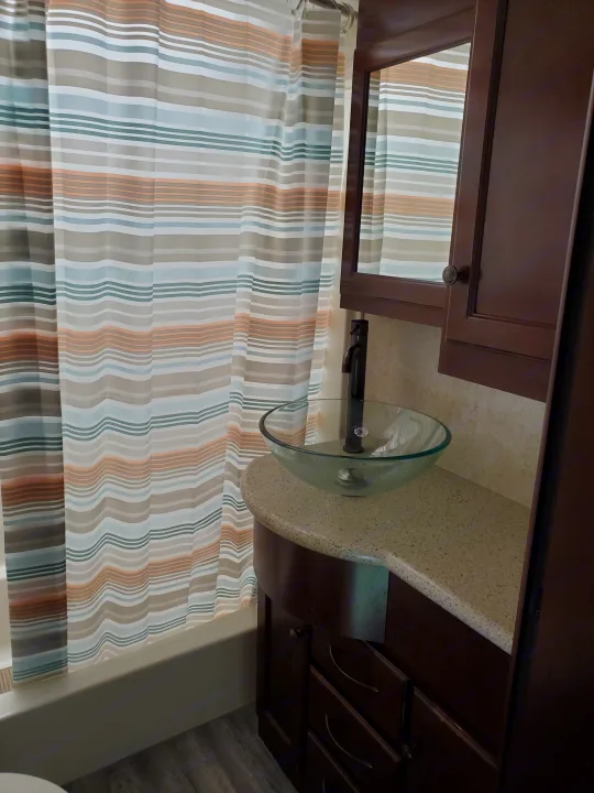 Inside an RV rental: a compact bathroom with a colorful striped shower curtain, clear glass vessel sink, and dark wood vanity.. Heartland Cyclone 2014