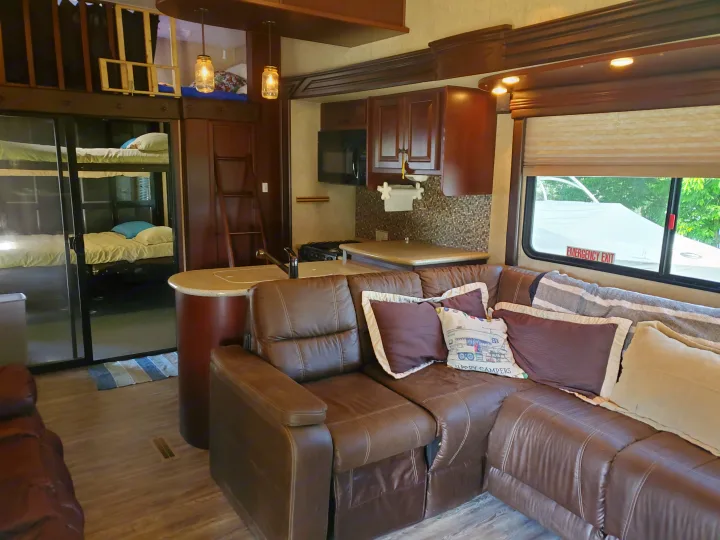 Spacious RV rental interior featuring a brown sectional couch, full kitchen, bunk beds, and an upstairs sleeping loft.. Heartland Cyclone 2014