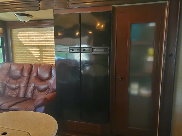 Inside an RV rental: a black refrigerator, brown leather sofa, window with blinds, and cabinet.. Heartland Cyclone 2014