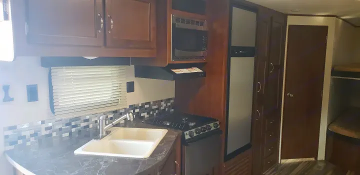 RV rental interior: A compact kitchen with sink, stove, microwave, fridge, and bunk beds visible on the right.. Jayco Jay Flight 2019