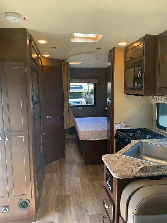 View inside an RV rental, highlighting the kitchen (sink, stove, microwave), main living area, and a bed in the private rear bedroom.. Thor Motor Coach Four Winds 2020
