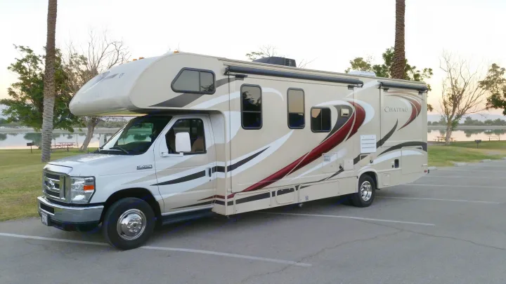 This Class C RV rental, a Chateau motorhome, is parked by a scenic lake at sunset, ready for outdoor adventures.. Thor Motor Coach Chateau 29G 2016