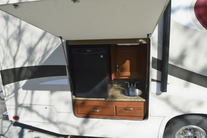 This RV rental features an outdoor kitchen in an open compartment with a mini-fridge, sink, and counter for camping.. Thor Motor Coach Chateau 29G 2016