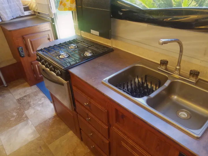 Compact RV rental kitchen with stove, oven, and double sink. Features wood cabinets & tiled floor, perfect for travel.. Forest River Rockwood Premier 2013