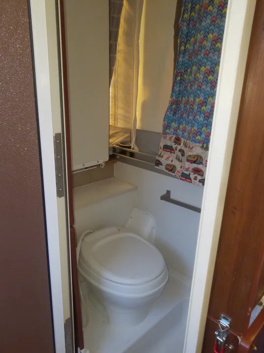 Compact RV rental bathroom with white toilet, small shelf, and colorful patterned shower curtain, perfect for camper travel.. Forest River Rockwood Premier 2013