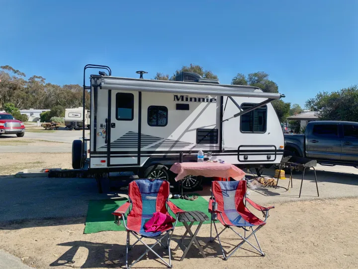 Minnie RV rental at a sunny campground with outdoor chairs and a picnic table, perfect for a relaxing getaway.. Other Other 2019
