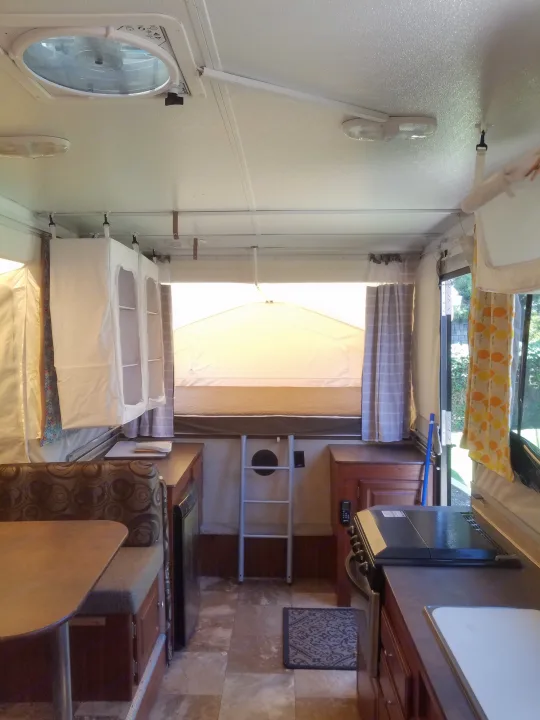 An inviting RV rental pop-up camper interior, showcasing a dinette, kitchen, and sleeping area with a ladder.. Forest River Rockwood Premier 2013