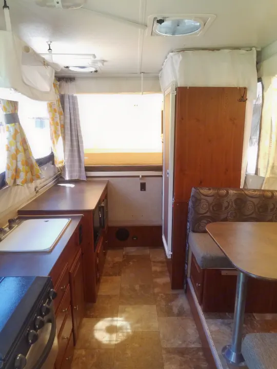RV rental interior: A compact kitchen with stove, sink, and microwave. Also shows dining area & bed in a pop-up camper.. Forest River Rockwood Premier 2013