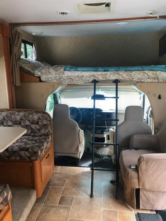 Interior of an RV rental: view from rear, showing cab-over bed, driver's area, dinette (left), & armchair (right).. ForestRiver Sunseeker 2012