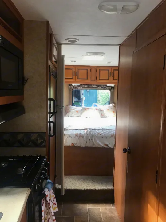 Inside an RV rental: kitchen appliances on left, hallway to raised bedroom with patterned bedding.. ForestRiver Sunseeker 2012