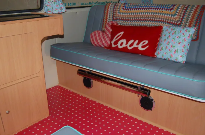 Inside a vibrant RV rental: light wood cabinets, gray upholstered seating with blue trim, and a playful red polka dot floor.. Volkswagen 2.0L T2 Late Bay 1975
