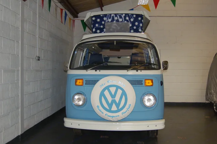 A classic blue and white VW pop-top camper van, a perfect RV rental from Retro Campers Norfolk, featuring a unique spare wheel cover.. Volkswagen 2.0L T2 Late Bay 1975