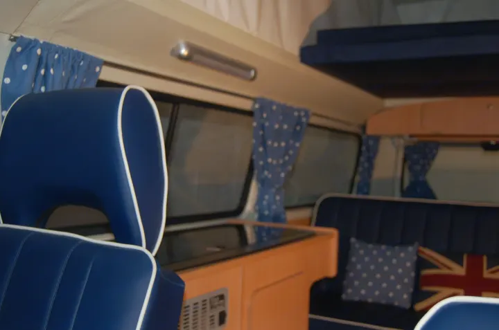 Inside a modern blue RV rental featuring comfortable seating, a compact kitchen setup, overhead bed, and polka-dot curtains.. Volkswagen 2.0L T2 Late Bay 1975