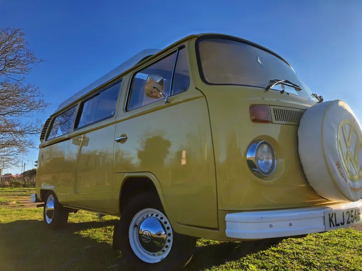 Experience freedom in this vintage pale yellow VW camper van, ideal for your next RV rental adventure. Parked on grass.. Volkswagen 2.0L T2 Late Bay 1975