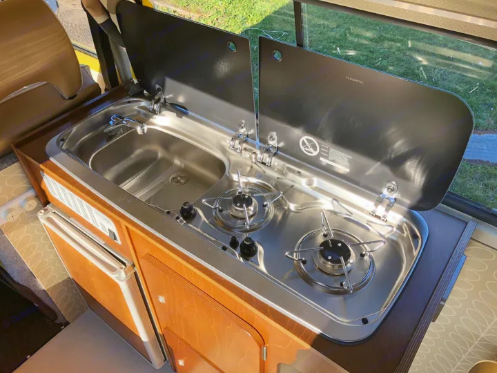 Inside an RV rental, this Dometic kitchen unit features a stainless steel sink, two-burner stove, faucet, and compact fridge.. Volkswagen 2.0L T2 Late Bay 1975