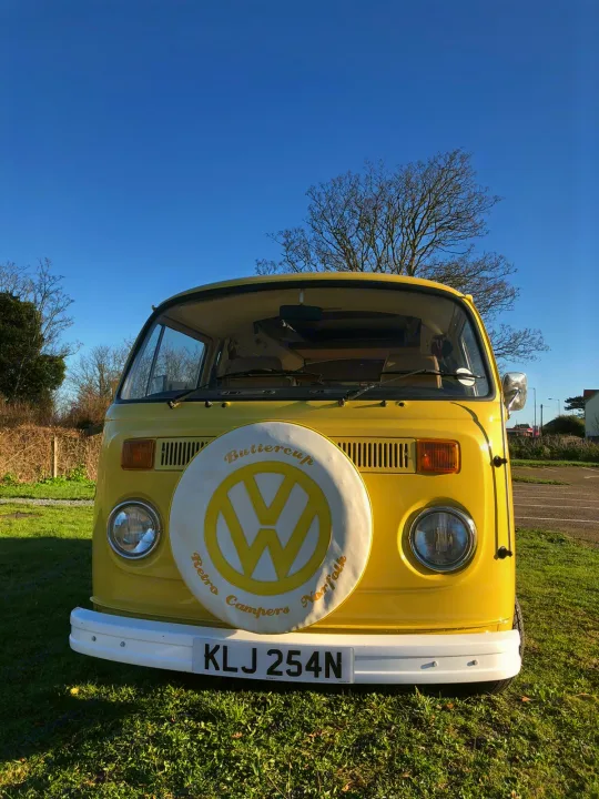 A cheerful yellow retro VW camper van, "Buttercup," parked on grass under a clear blue sky. Perfect for an RV rental.. Volkswagen 2.0L T2 Late Bay 1975